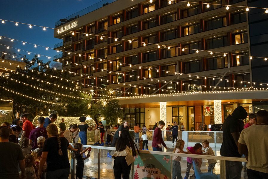 A lively outdoor ice rink at night, surrounded by festive lights and a modern building