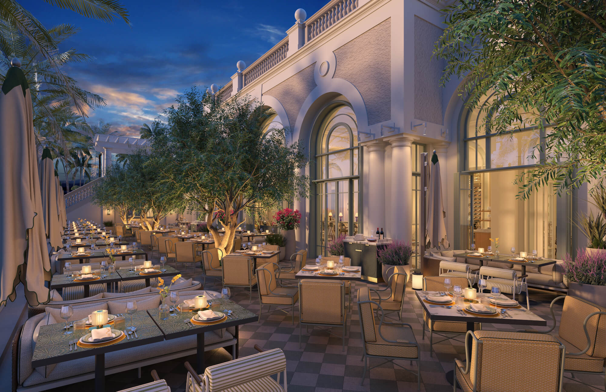 An elegant outdoor restaurant with long tables set for dinner, surrounded by lush greenery and illuminated by soft lighting at dusk