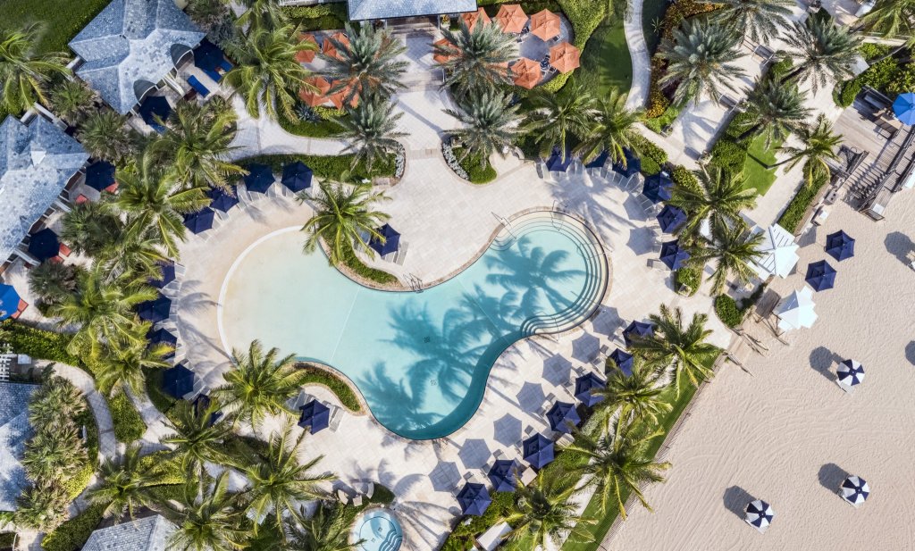 Vista aérea de un lujoso complejo turístico tropical con una gran piscina sinuosa rodeada de palmeras y cabañas