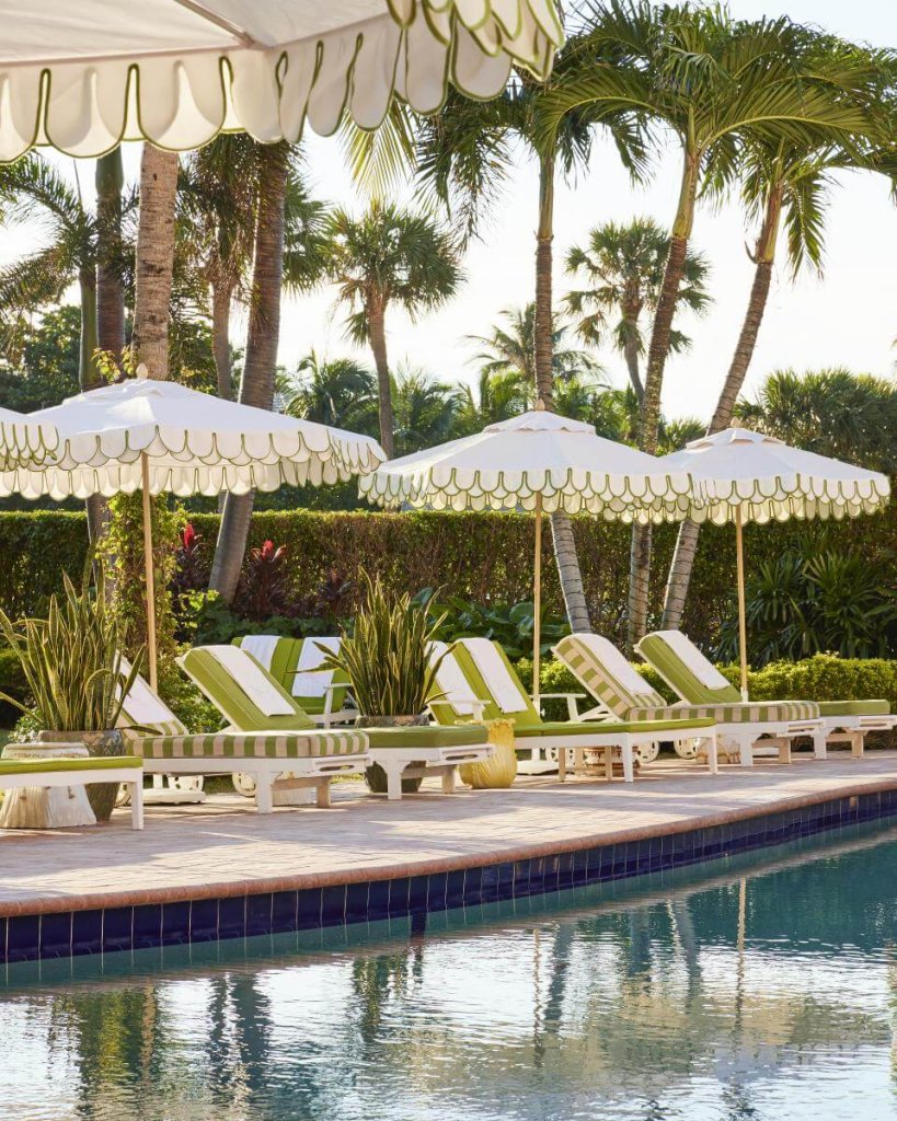 Une oasis de sérénité au bord de la piscine avec des parasols à rayures blanches et vertes ombrageant des chaises longues entourées d'une végétation tropicale luxuriante et de palmiers.