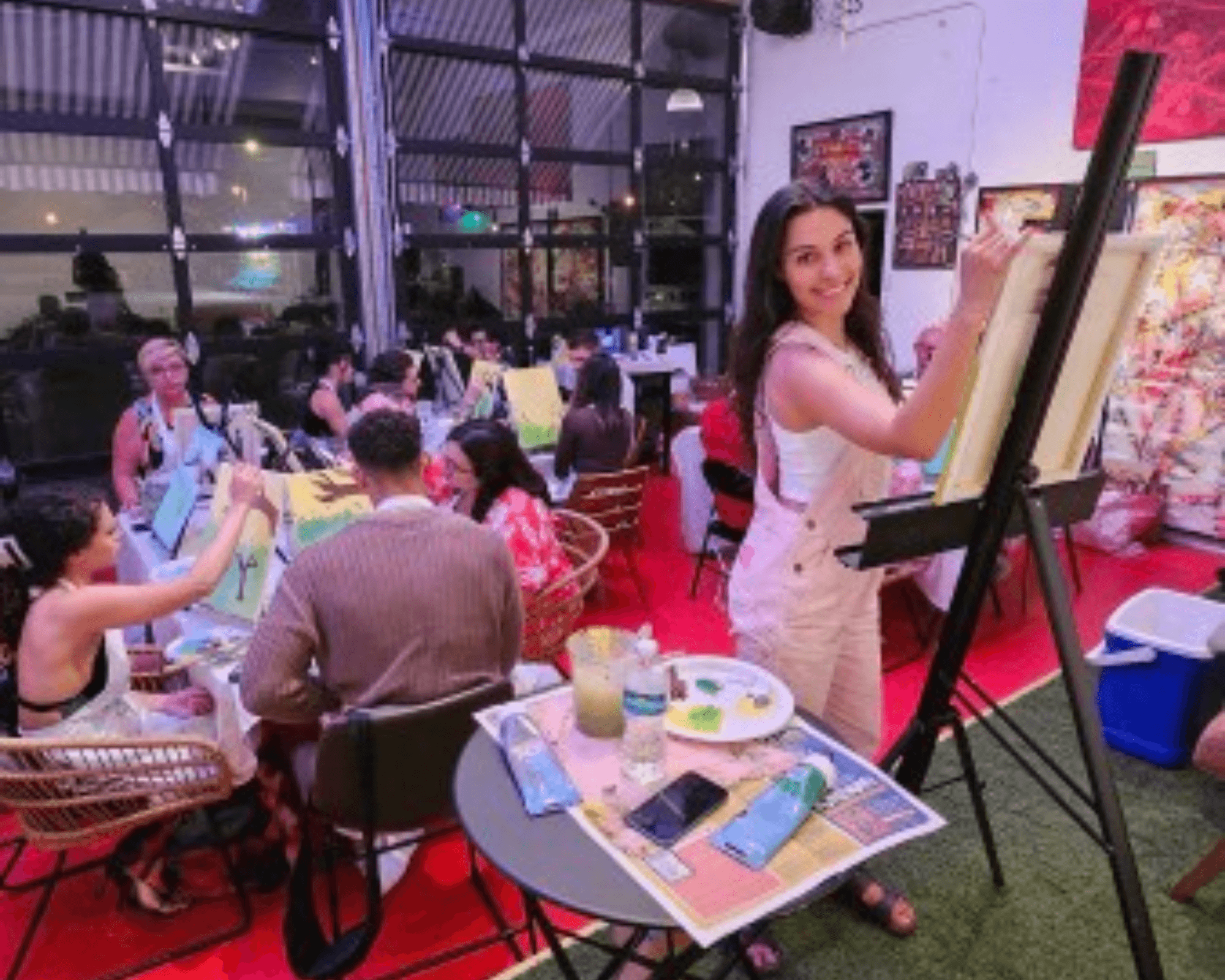 A lively paint-and-sip event with a group of people seated around tables, painting on canvases while enjoying drinks and conversation
