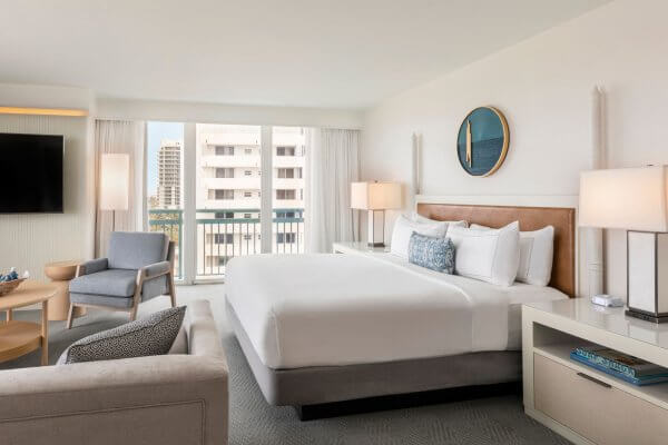 Una moderna suite de hotel con cama king-size, zona de estar y balcón con vistas al paisaje urbano