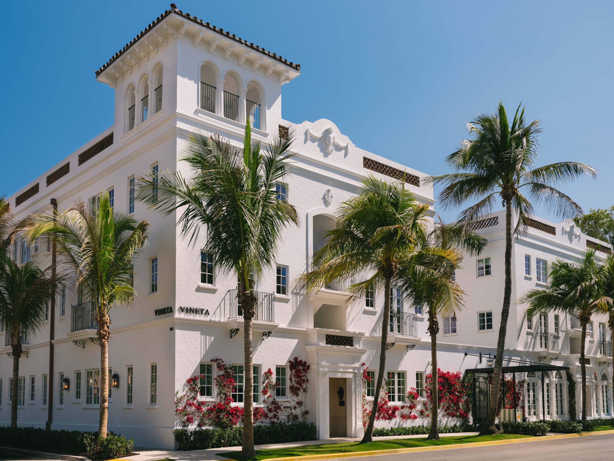 A stunning white Mediterranean-style building with red flowers and palm trees in a tropical setting