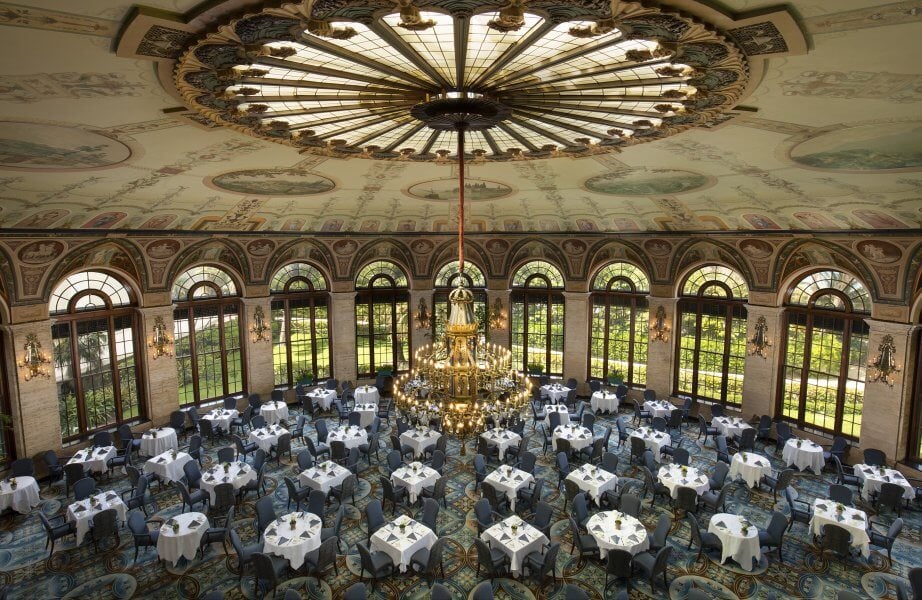 Une salle à manger ornée d'un grand lustre et de fenêtres cintrées donnant sur des jardins luxuriants.