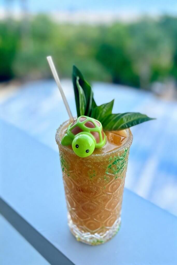Um vibrante coquetel tropical decorado com um brinquedo de tartaruga verde e folhas de manjericão fresco, servido em um copo texturizado com canudo