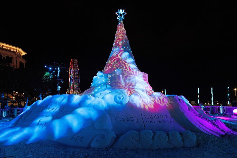 A vibrant, illuminated Christmas tree made of sand, standing tall against the night sky, with colorful projections and a star on top