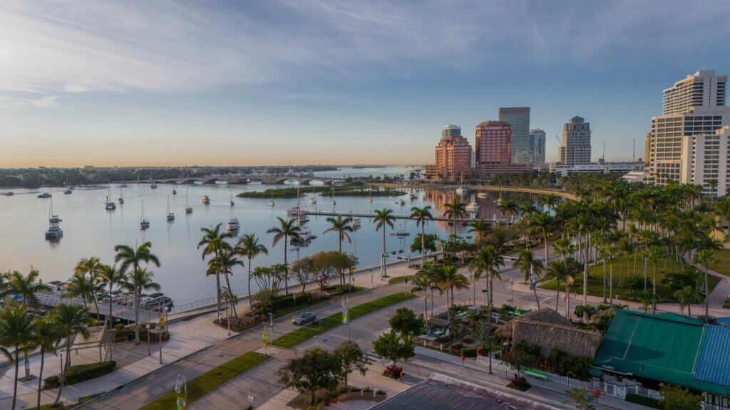 Ein Panoramablick auf eine belebte Stadt am Wasser mit hohen Gebäuden, Palmen und zahlreichen Booten in der Bucht bei Sonnenuntergang