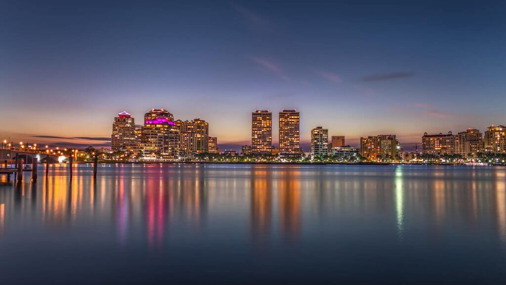 A serene waterfront view of a city skyline at dusk, with reflections shimmering on the calm water