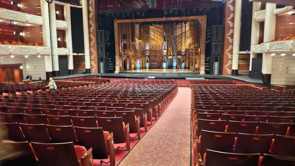 Un grand théâtre avec des rangées de sièges rouges menant à une scène avec une toile de fond ornée.