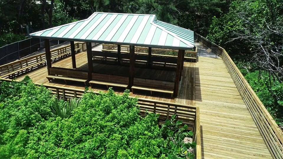 An elevated wooden deck with a striped roof pavilion surrounded by lush greenery and a wooden railing