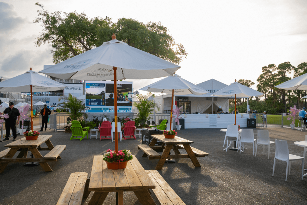 Les tables de pique-nique en bois, les chaises Adirondack colorées et les parasols portant la marque "The Palm Beaches" sont installés à l'extérieur du Cognizant Classic.