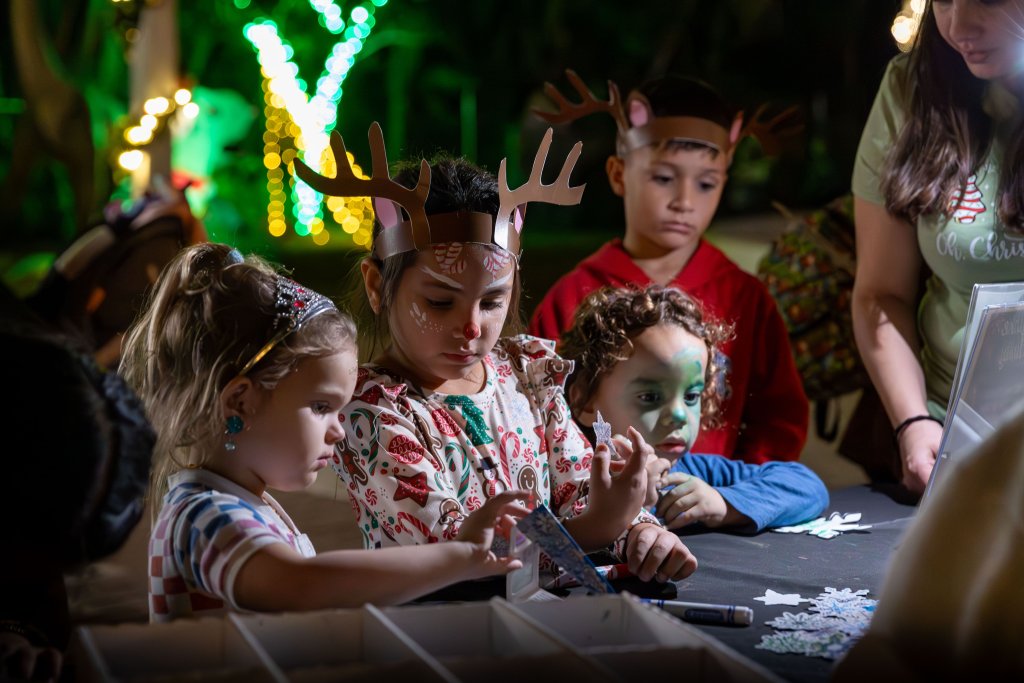 Kinder in weihnachtlichen Kostümen und mit Gesichtsbemalung beschäftigen sich bei einer festlichen Veranstaltung mit einer Bastelarbeit