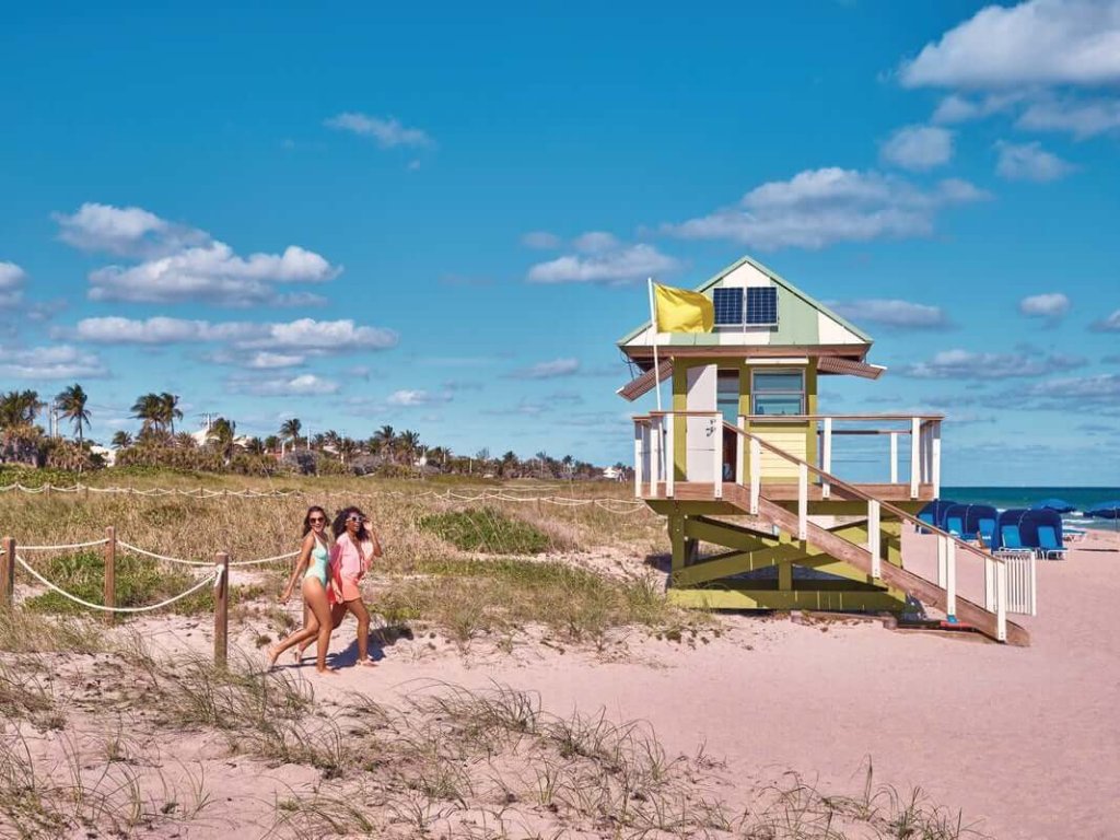 Two women walking along the sandy beach near a lifeguard tower in Delray Beach