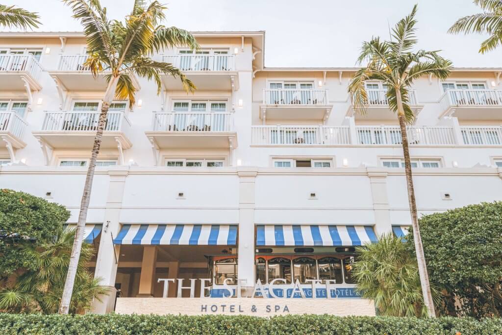 A luxurious beachfront hotel with white balconies and blue and white striped awnings, surrounded by palm trees and lush greenery