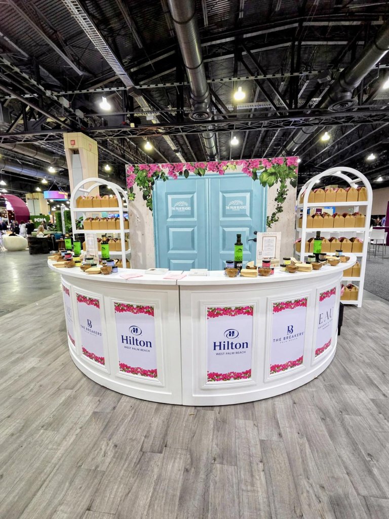 Un stand de feria de Hilton West Palm Beach con la marca, decoración floral y estantes