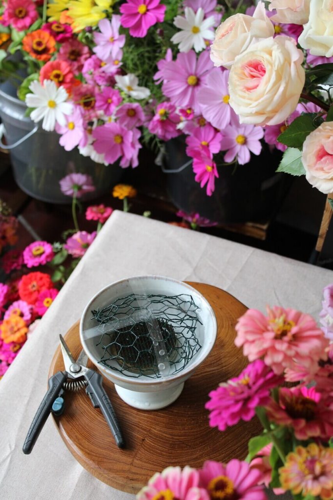 um arranjo de flores com uma tesoura e uma tigela de água