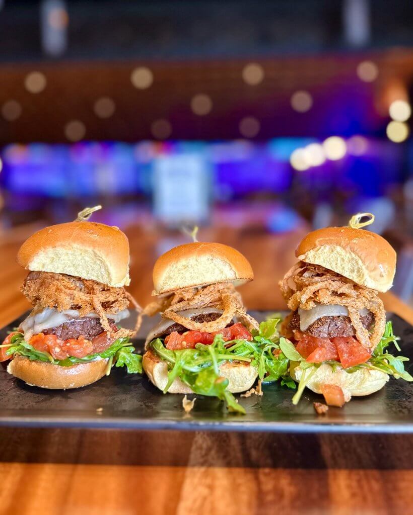 Tres deliciosas minihamburguesas con tiras de cebolla crujiente, queso fundido y rúcula fresca en un plato negro