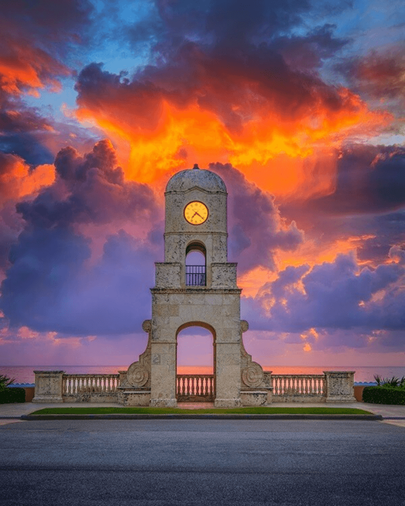 A majestic stone clock tower stands tall against a breathtaking sunset sky, with vibrant orange and purple clouds creating a dramatic backdrop