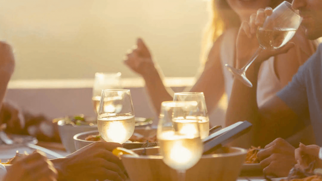 Un grupo de amigos disfrutando de una comida juntos, brindando con copas de vino blanco