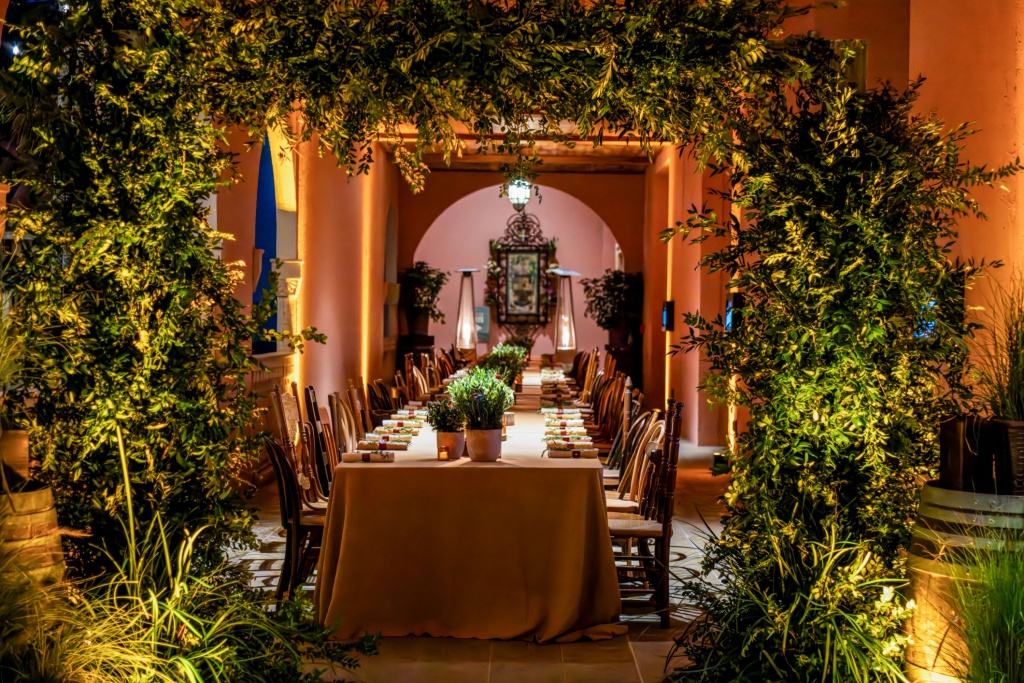 Un elegante comedor al aire libre bajo un frondoso arco verde, iluminado por una luz tenue