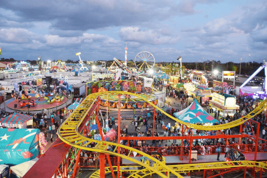 A bustling amusement park at dusk, filled with colorful rides, games, and crowds of excited visitors