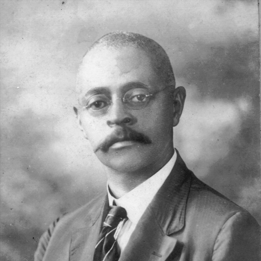 A dignified African American man with glasses and a mustache, dressed in a formal suit and tie