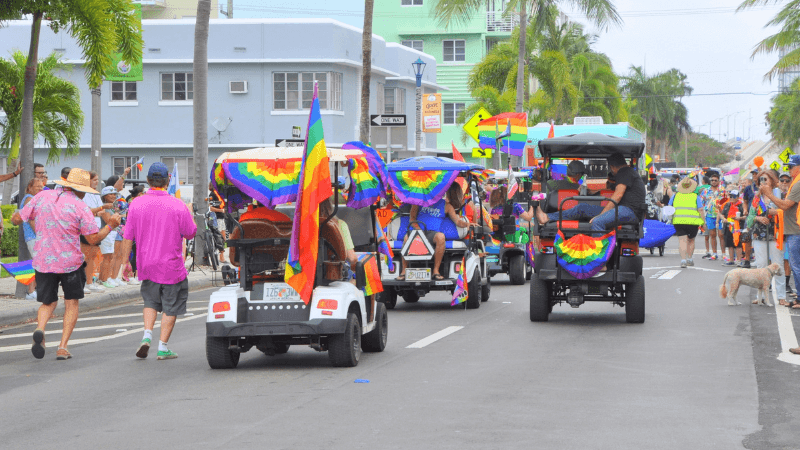 A vibrant Pride parade featuring colorful golf carts adorned with rainbow flags and enthusiastic participants lining the streets