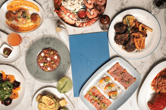 A variety of colorful and appetizing dishes, including seafood, meat, and vegetarian options, are artfully arranged on a marble table