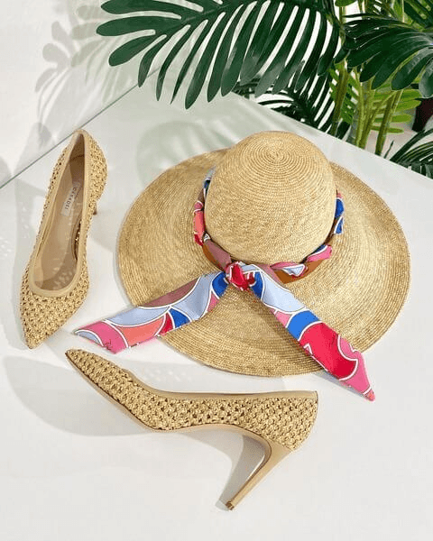 Um conjunto elegante com sapatos de salto alto bege trançados, um chapéu de palha de aba larga adornado com um lenço colorido e vibrante e uma planta verde exuberante ao fundo