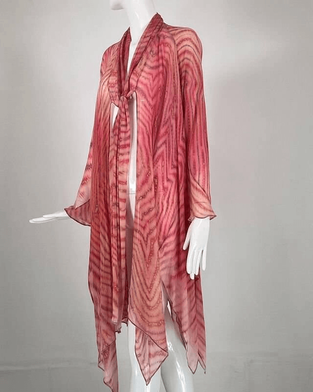 Um manequim envolto em um xale tie-dye rosa e vermelho vibrante e fluido, com uma textura transparente e arejada