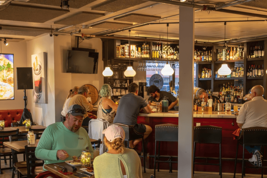 Patrons enjoy drinks and meals at a lively bar with a well-stocked liquor shelf and cozy seating