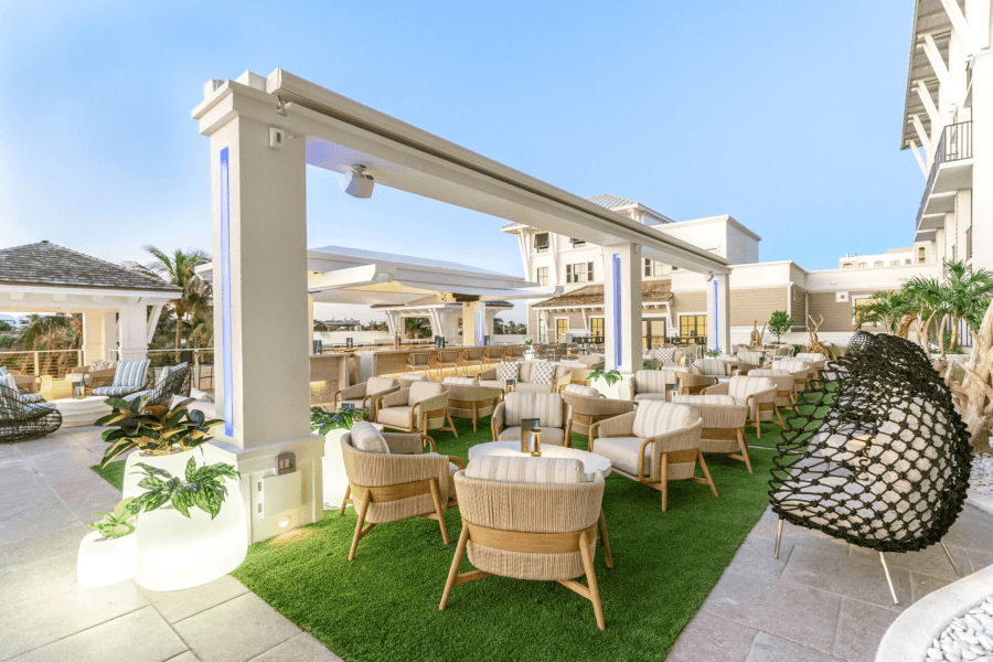 A luxurious rooftop lounge with a modern design, featuring comfortable seating, lush greenery, and a stunning view of the surrounding buildings and clear blue sky