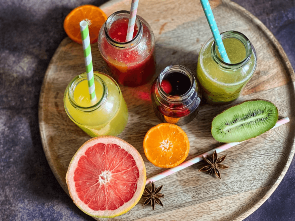 A variety of colorful fruit juices and smoothies with fruit slices and star anise on a wooden tray
