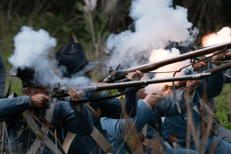 Une ligne de soldats en uniformes bleus tirent avec leurs mousquets, créant une scène dramatique avec des volutes de fumée et des flammes.