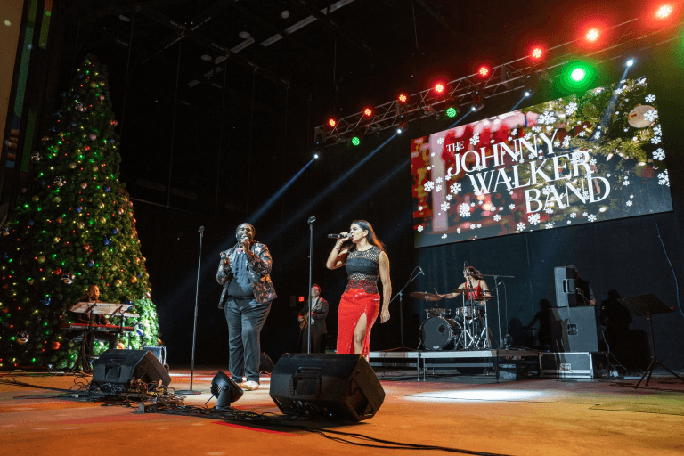 A festive concert featuring The Johnny Walker Band performing on stage with a large Christmas tree in the background