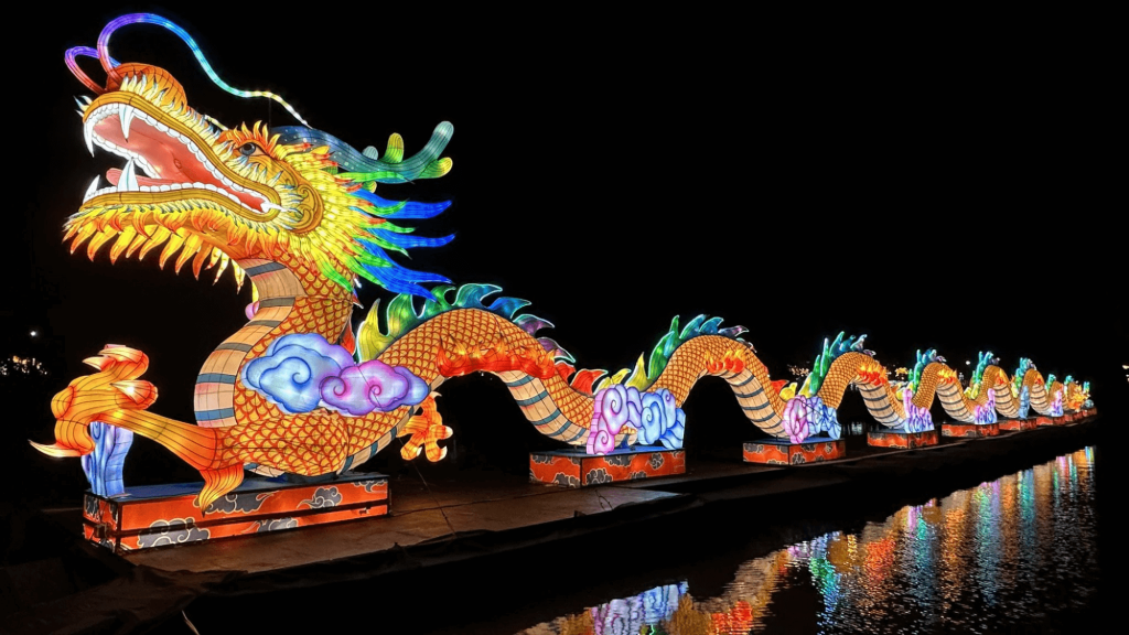 Une sculpture de danse du dragon illuminée et vibrante s'étend sur un plan d'eau sombre, ses écailles brillant dans un spectre de couleurs.