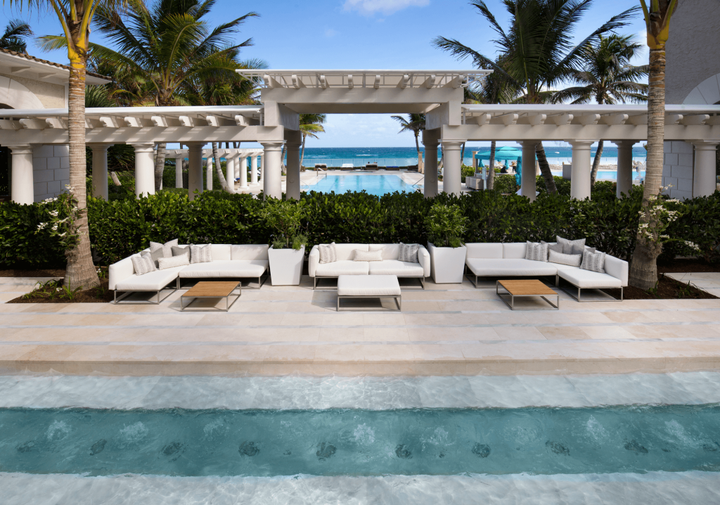 Une station tropicale sereine avec une pergola blanche, des palmiers et une piscine surplombant l'océan.