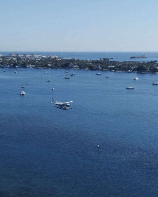 A seaplane floats on calm waters surrounded by boats and a distant shoreline