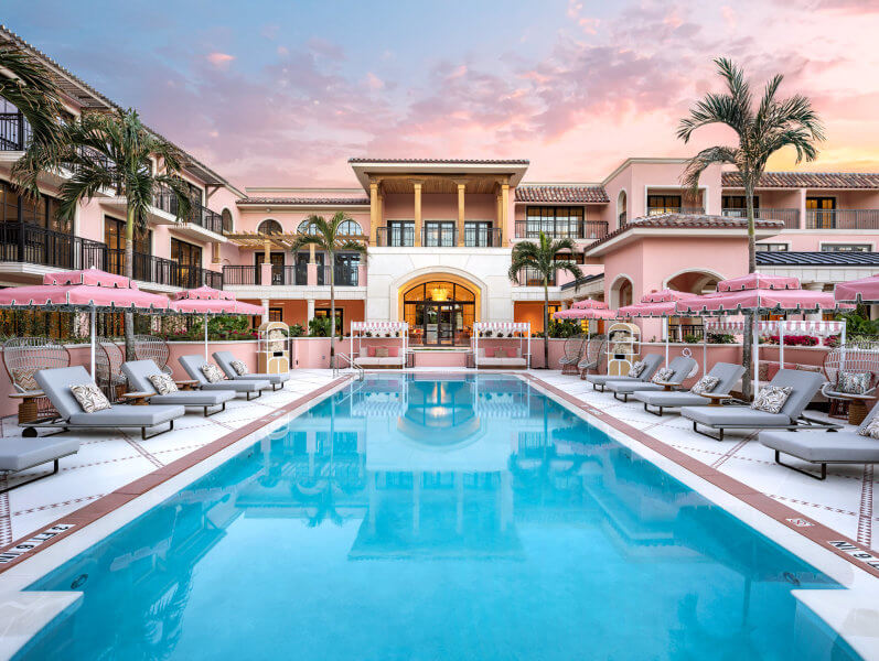 A luxurious pink resort building with a large swimming pool at sunset