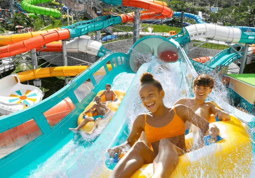 Group of teenagers laughing while riding yellow tubes down a large water park slide