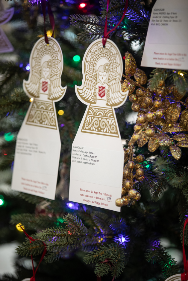 Nahaufnahme eines Weihnachtsbaums, der mit Engelsschildern der Heilsarmee geschmückt ist, auf denen jeweils der Name, das Alter, die Kleidergröße und Geschenkwünsche eines Kindes angegeben sind und die zu Weihnachtsspenden für bedürftige Kinder aufrufen