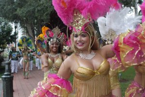 Un carnaval de rue vibrant avec des artistes en costumes élaborés or et rose, ornés de plumes et de paillettes, qui dansent énergiquement.