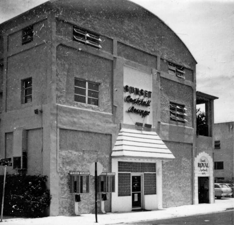 A black and white photograph of a building with a curved facade and a sign reading 'Sunset Cocktail Lounge' above the entrance