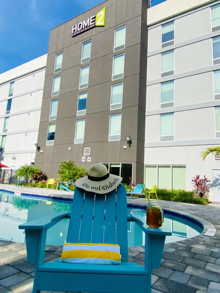 Una silla Adirondack azul con un sombrero y una toalla junto a la piscina de un hotel Home2 Suites by Hilton
