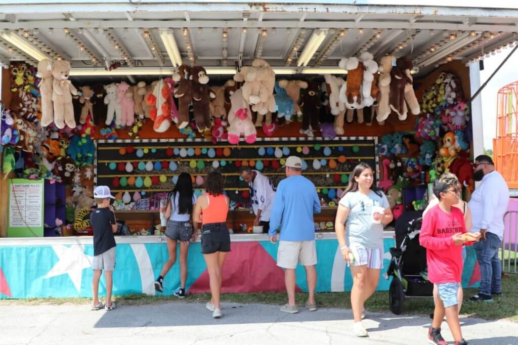 A lively carnival game booth brimming with colorful stuffed animals and prizes, attracting a crowd of excited children and adults